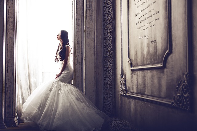 Nevesta vo svadobných šatách pozerá von cez veľké okno
