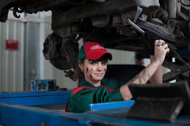Žena v zelených monterkách, špinavou tvárou od oleja opravuje auto