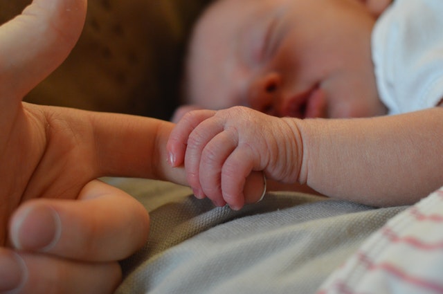 Spiaci novorodenec drží za ruku dospelého človeka